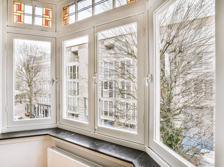 Bright bay window with white frames overlooking a city street and bare trees outside.