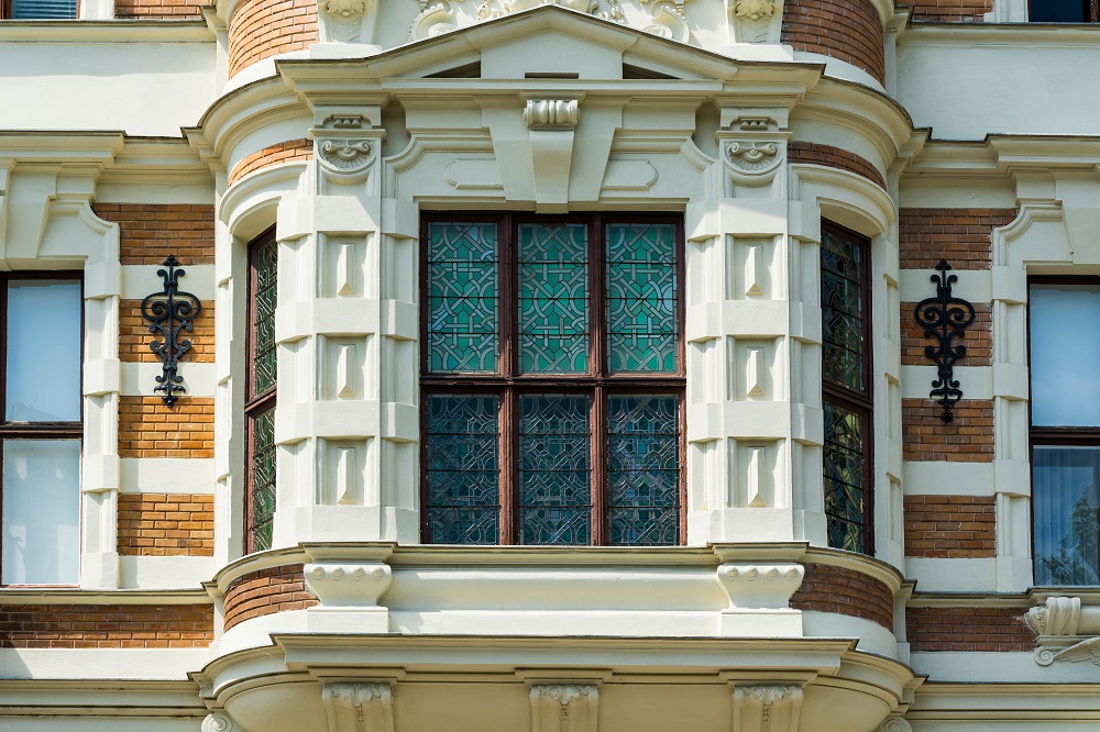 classic-facade-of-a-residential-building-in-the-au-2026-03-25-23-42-28-utc - BVG Curved bay window with lattice panes framed by cream stone on a brick building, with wrought-iron wall lamps on either side.