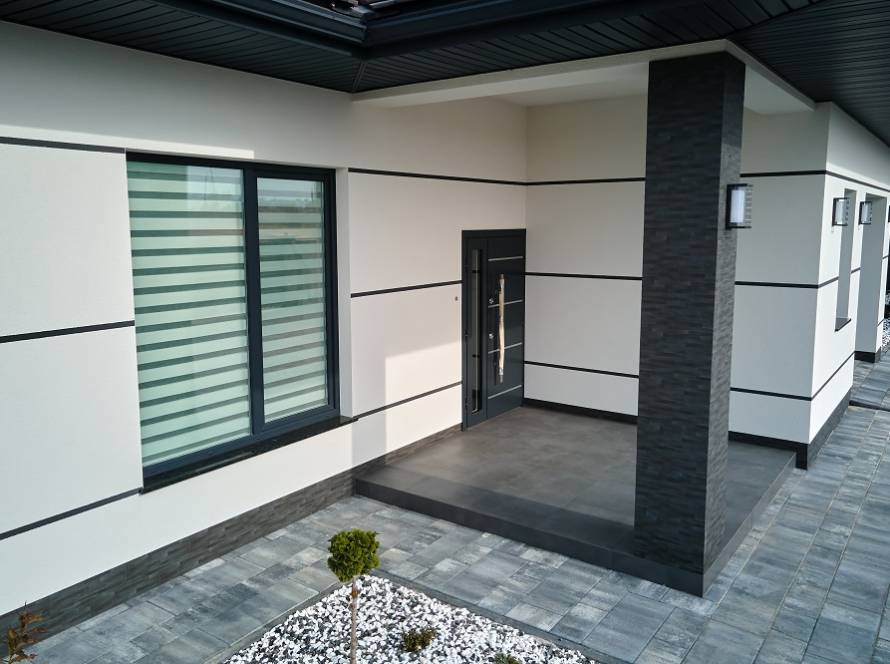 Modern house entrance with dark door under a covered porch, light walls with black trim, and a large window with frosted blinds to the left