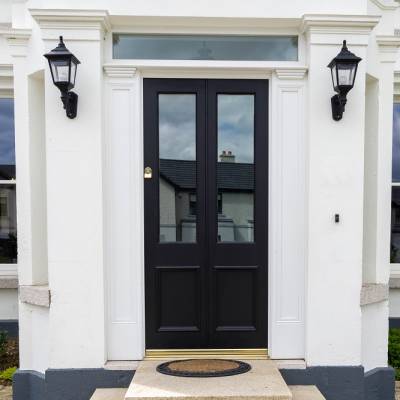 Black double front doors with glass panels, white trim, and two wall lanterns on each side of the entrance.