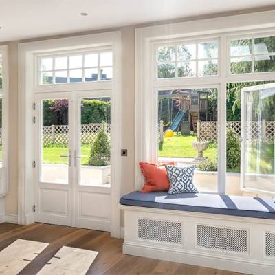 Bright living room with a built-in window seat under large multi-pane windows, overlooking a garden with a playset and fence.