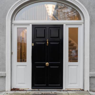 Front entrance with black paneled door, white trim, and a large arched window above; autumn leaves on the doorstep.