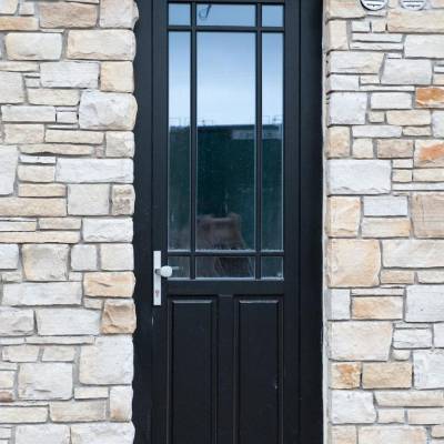 Black front door with glass panel windows set in a beige stone wall on an exterior façade.