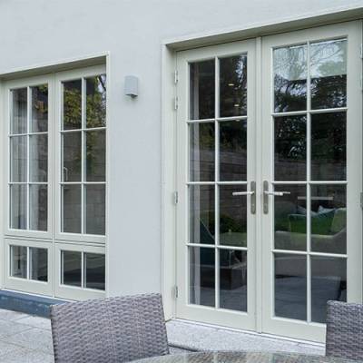 Cream-colored French doors with grid panes on an exterior wall, opening to a stone patio with wicker seating.