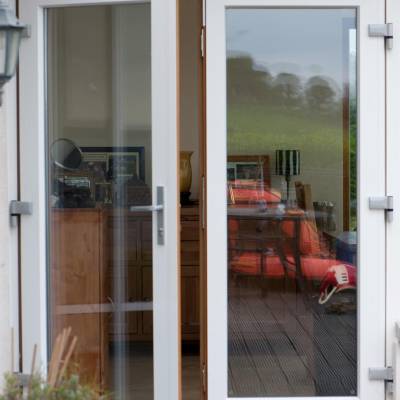Open glass patio doors showing a living room with wooden furniture, framed photos, and a red chair visible inside; an outdoor deck visible outside.
