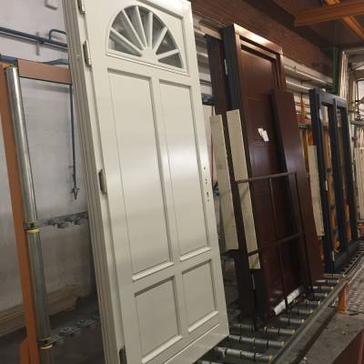 White exterior-panel door with a semicircular window on top stands on a metal roller rack in a doorway factory/warehouse setting.