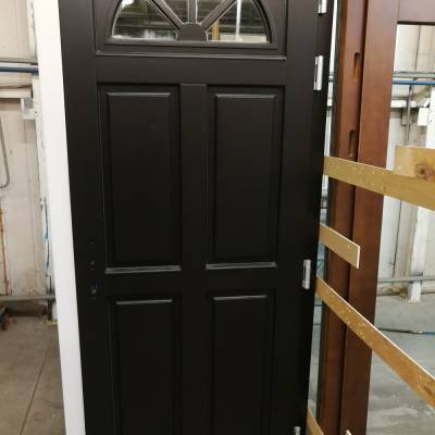 Black front door with a semicircular window at the top, placed upright in a warehouse setting.