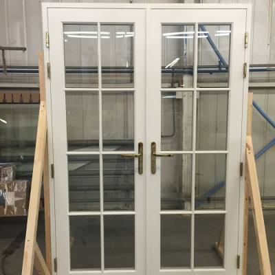 White French doors with grid-style glass panes and brass handles, propped in a workshop setting.