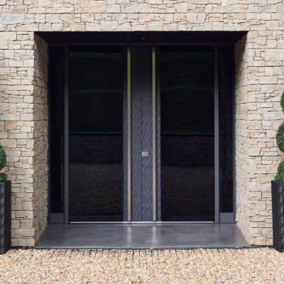 Stone building entrance with tall glass doors flanked by sculpted spiral topiary in black planters.